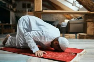 Middle Eastern man performing ritual prayer on the floor at home.
