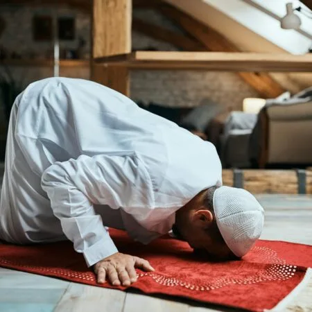 Middle Eastern man performing ritual prayer on the floor at home.
